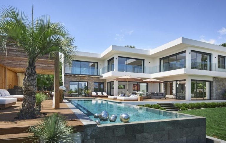Modern villa with pool, terrace and palm tree, surrounded by greenery.
