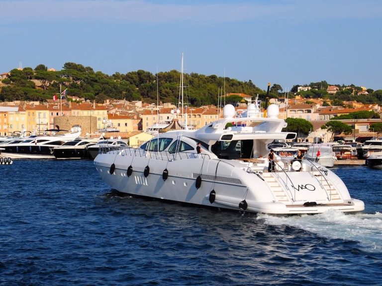 White yacht sailing in a harbor, surrounded by hills and boats.