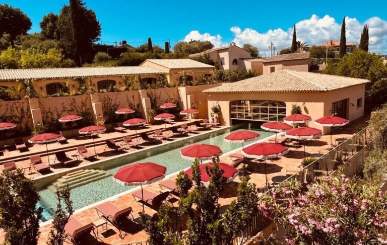 Open-air pool with loungers and red parasols, surrounded by greenery.
