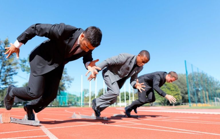 Three men in suits running on an athletics track.