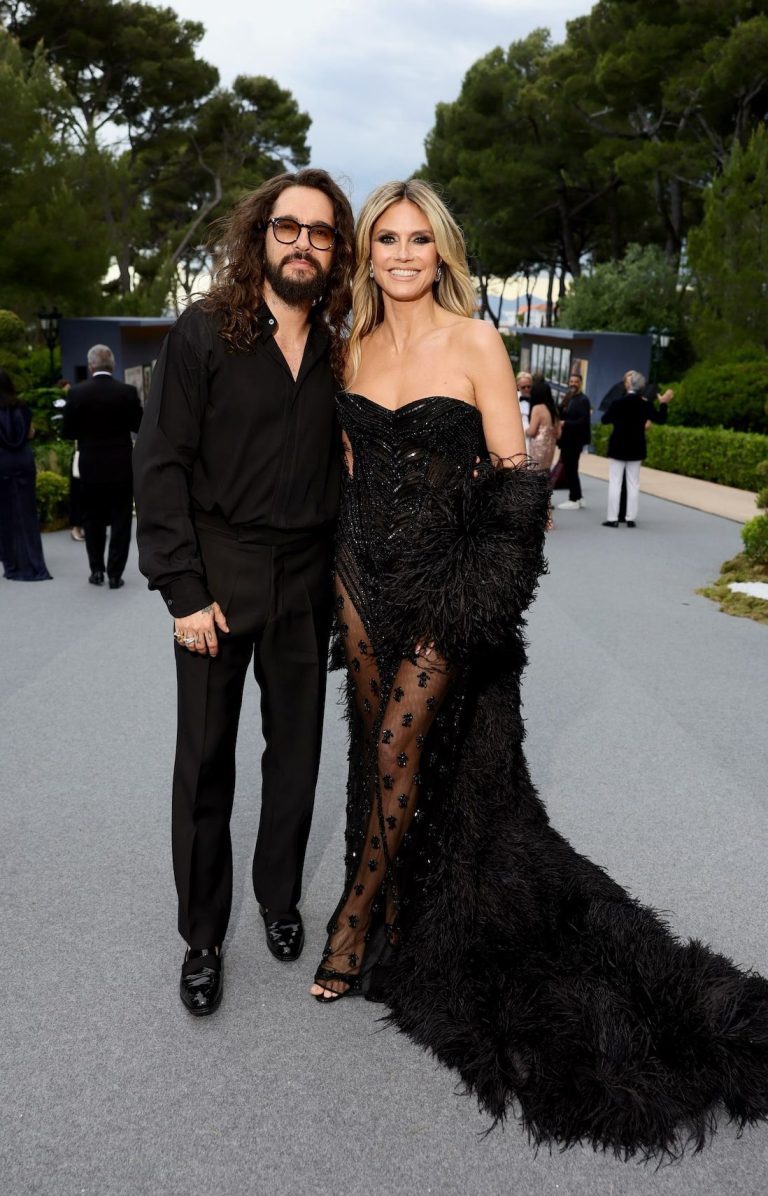 Two people dressed in black pose together at an outdoor event.