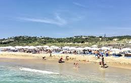 Sunny beach with umbrellas, bathers and dunes in the background.