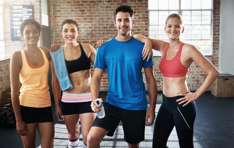 A group of four smiling sportsmen and women in a gym.
