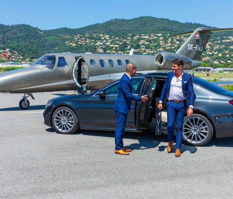 Man in suit getting out of a car, near a private jet on a runway.