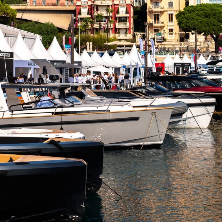 Sailboats and yachts moored in a bustling harbor, surrounded by white tents.