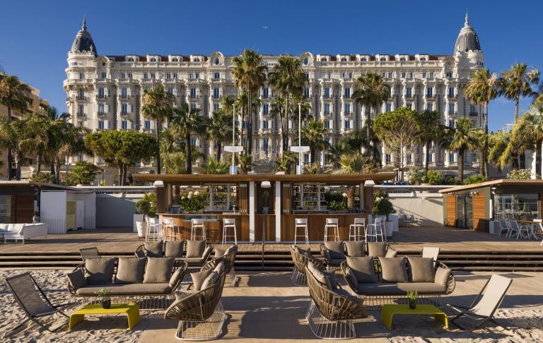 Blog Black Diamond Holding Group Emblematic hotel with sun loungers on the beach, surrounded by palm trees.