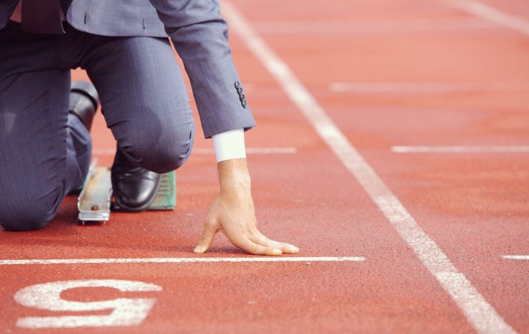 A man in a suit prepares to run on an athletics track.