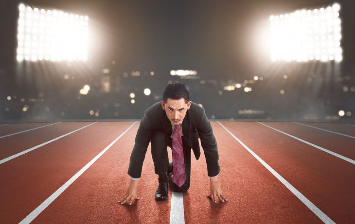 Man in suit ready to run on an athletics track, illuminated by spotlights.